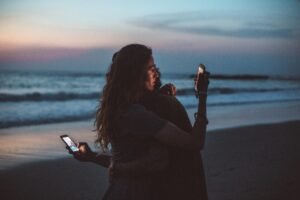 two people looking at their phones while hugging